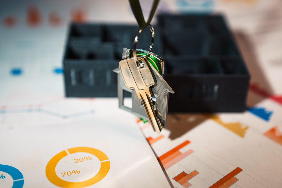 House keys on a house-shaped keychain hanging above financial charts and a model home, representing rental property investment analysis